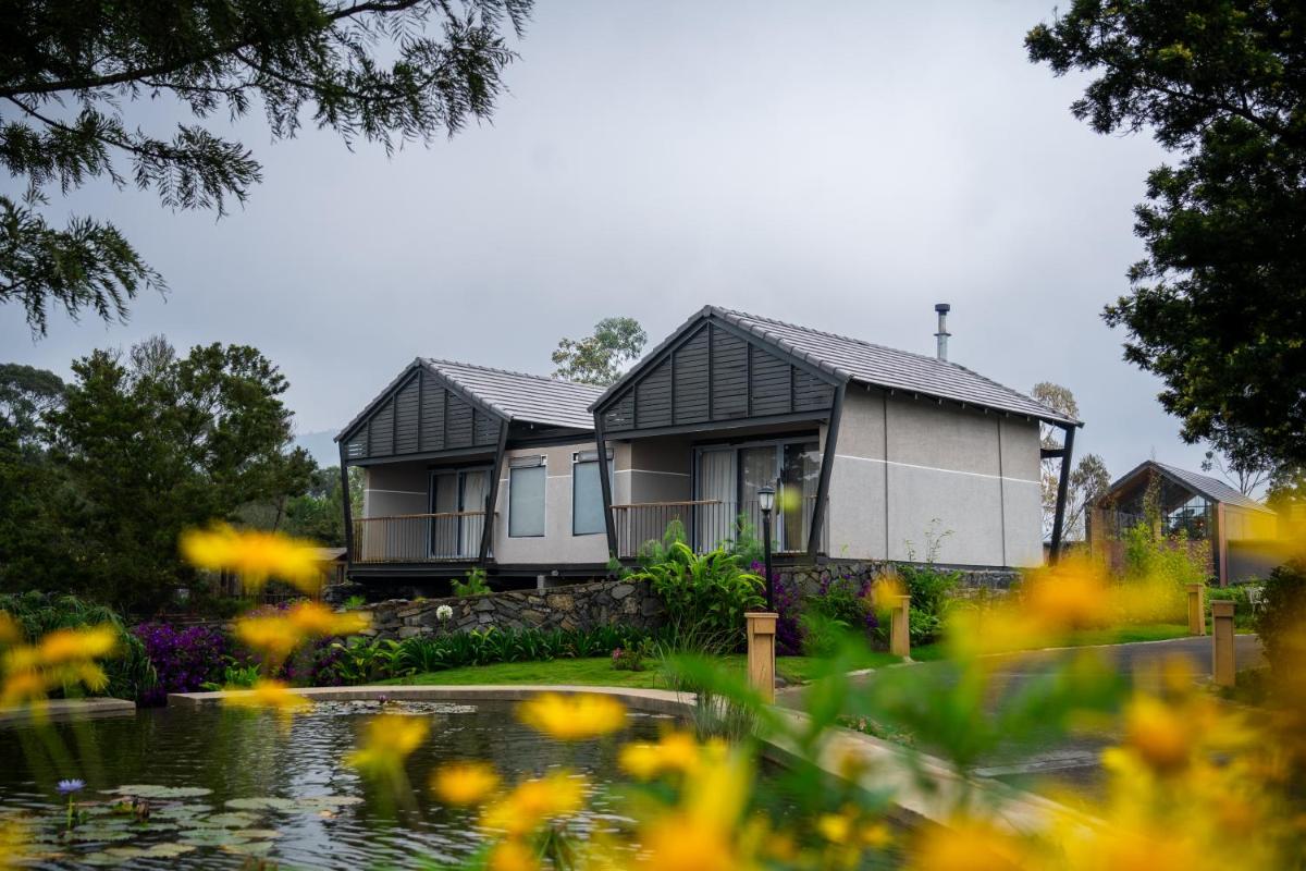 a house with a pond and flowers in the foreground at WelcomHeritage Ayatana Ooty in Ooty