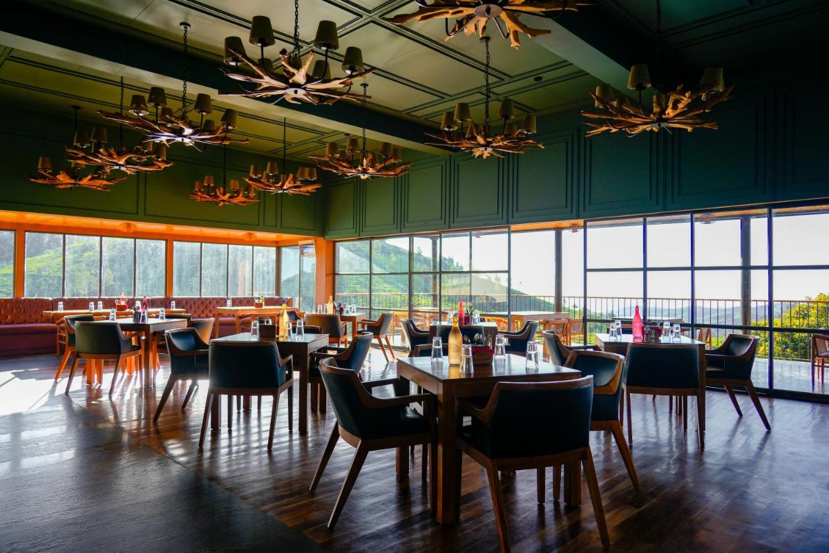 a restaurant with tables and chairs and large windows at WelcomHeritage Ayatana Ooty in Ooty