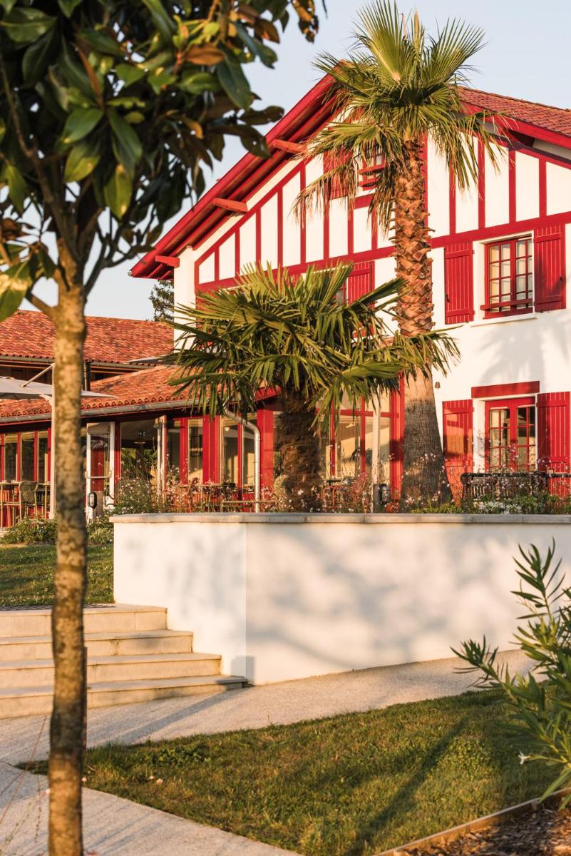 un bâtiment rouge et blanc avec des palmiers devant dans l'établissement Hôtel INDARRA & SPA - Piscine, à Arbonne