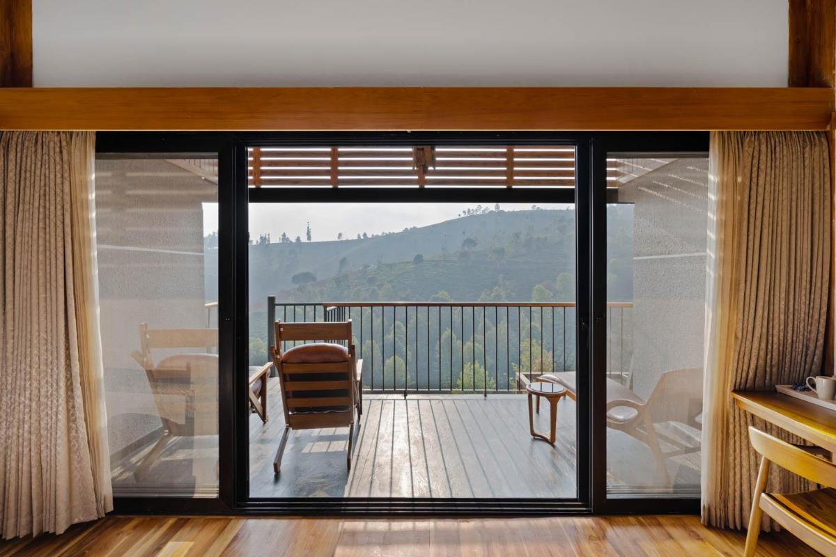 a living room with sliding glass doors to a deck at WelcomHeritage Ayatana Ooty in Ooty