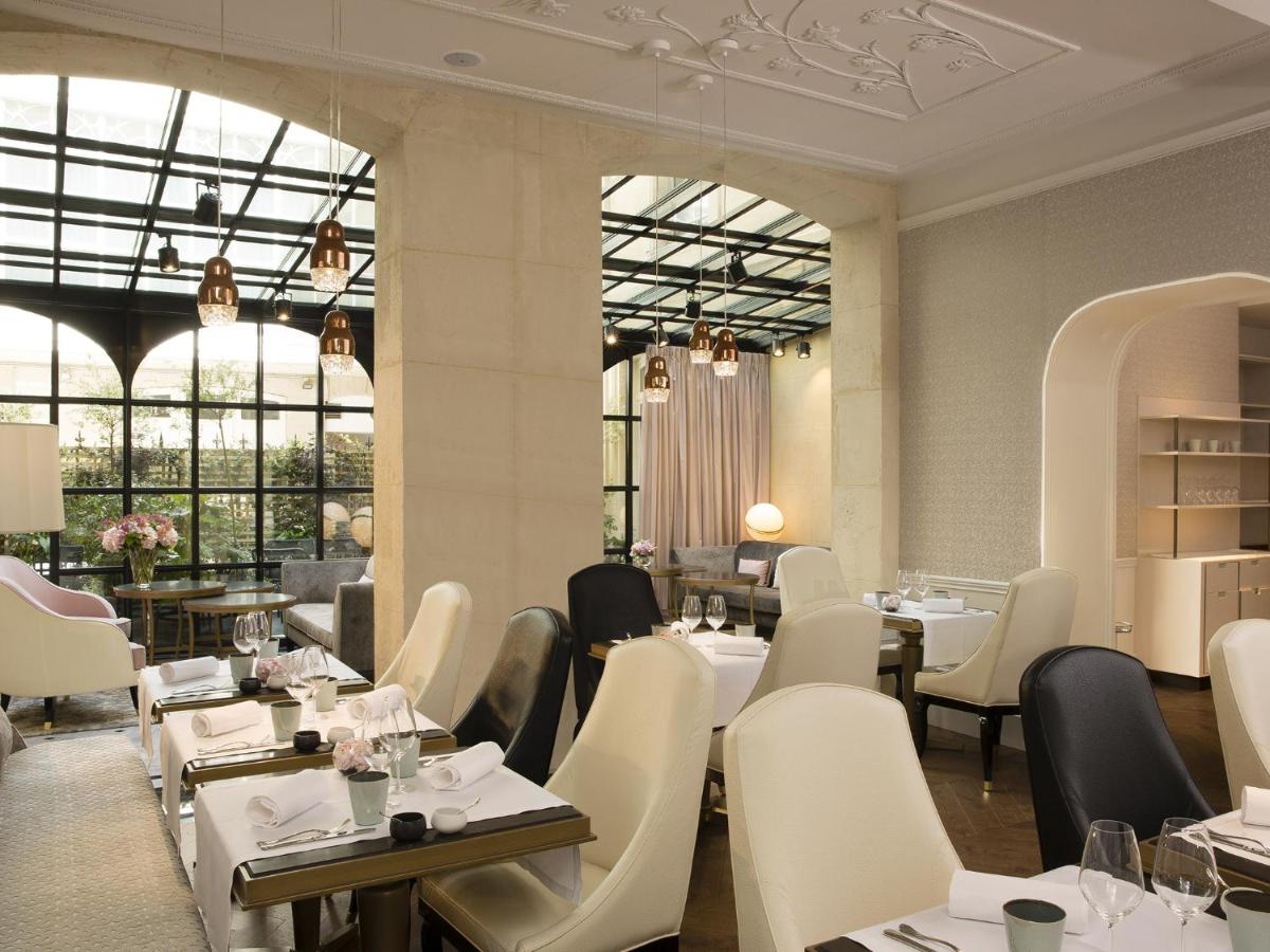 un restaurant avec des tables et des chaises blanches et des fenêtres dans l'établissement Le Narcisse Blanc, à Paris