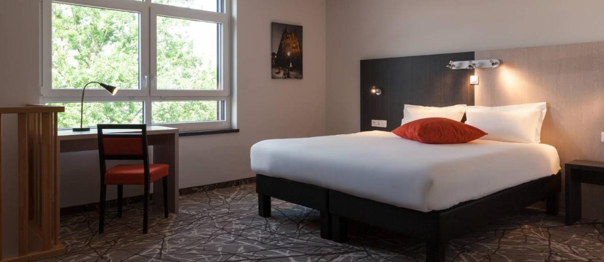 Cette chambre comprend un lit, un bureau et une fenêtre. dans l'établissement The Originals Boutique, Hôtel d'Alsace, Strasbourg Sud, à Illkirch-Graffenstaden
