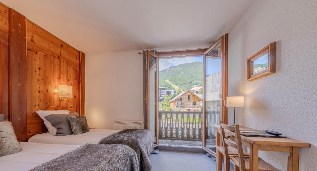 une chambre avec deux lits et une grande fenêtre dans l'établissement Logis Hôtel et Spa Le Christiania, à La Salle Les Alpes