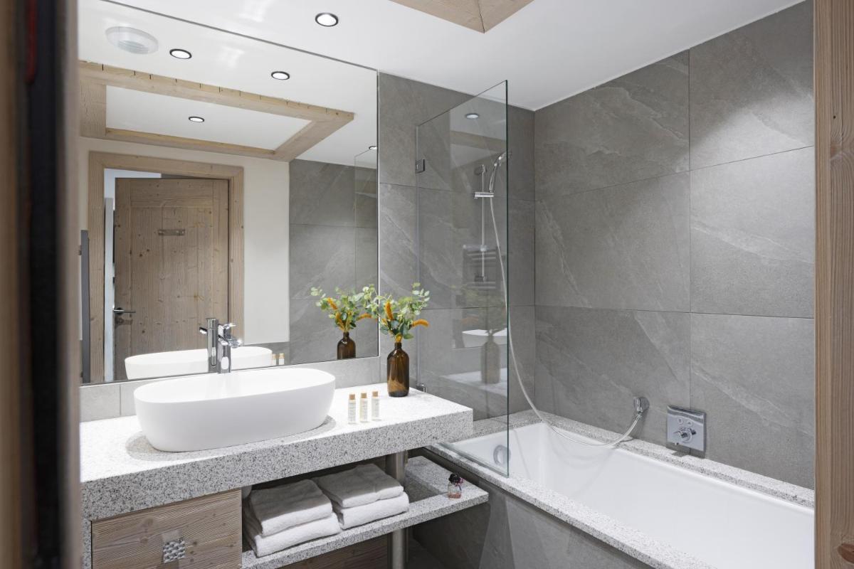 une salle de bain avec un lavabo, une baignoire et un miroir dans l'établissement MGM Hôtels & Résidences - Résidence Chalets de Joy, au Grand-Bornand