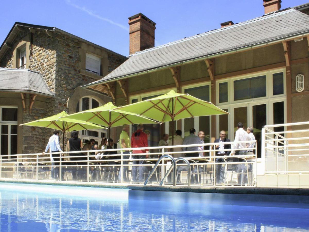 un groupe de personnes debout autour d'une piscine avec des parasols dans l'établissement Mercure Saint Nectaire - Spa & Bien-Être, à Saint-Nectaire
