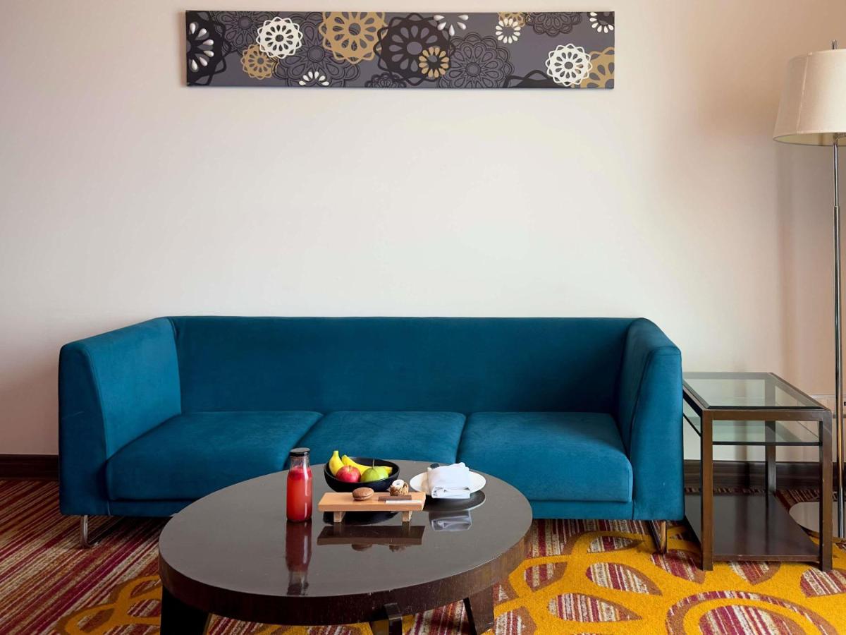 a living room with a blue couch and a table at Novotel Pune Viman Nagar Road in Pune