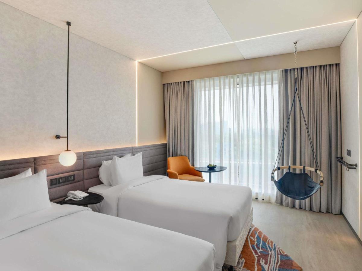 a hotel room with two beds and a window at Novotel Pune Viman Nagar Road in Pune