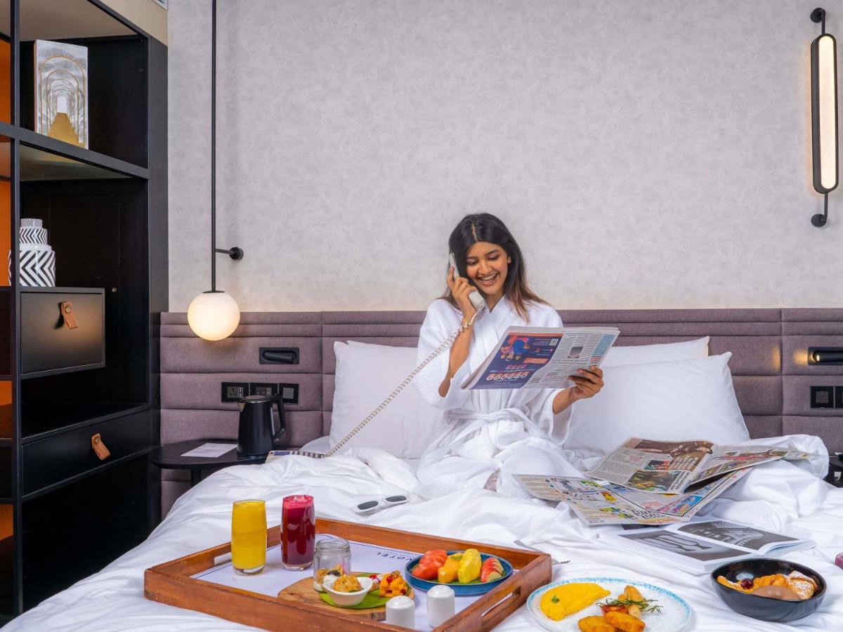 a woman sitting in bed talking on a cell phone at Novotel Pune Viman Nagar Road in Pune
