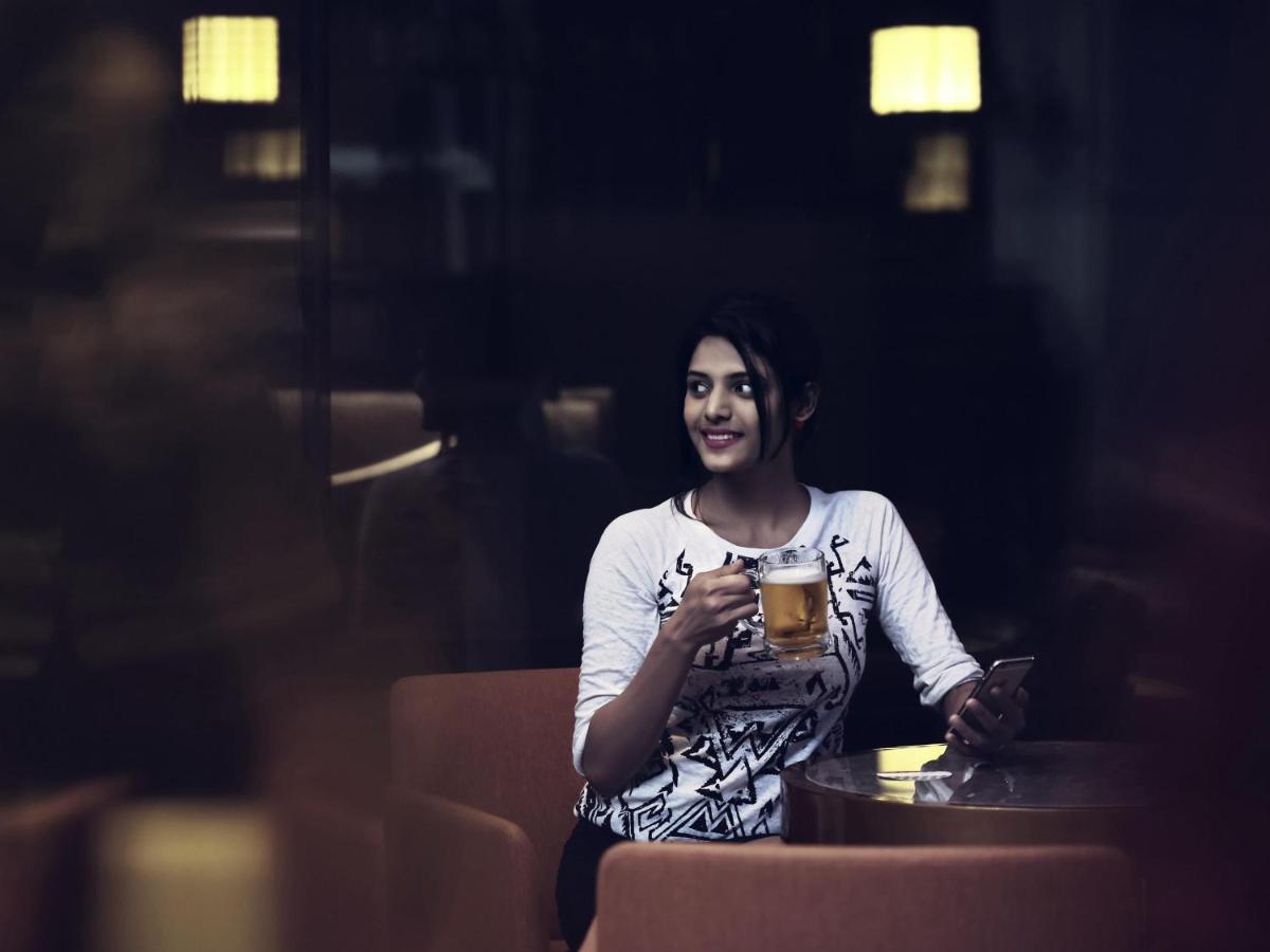 a woman sitting at a table holding a drink at Mercure Hyderabad KCP Banjara Hills, An Accor Hotel in Hyderabad