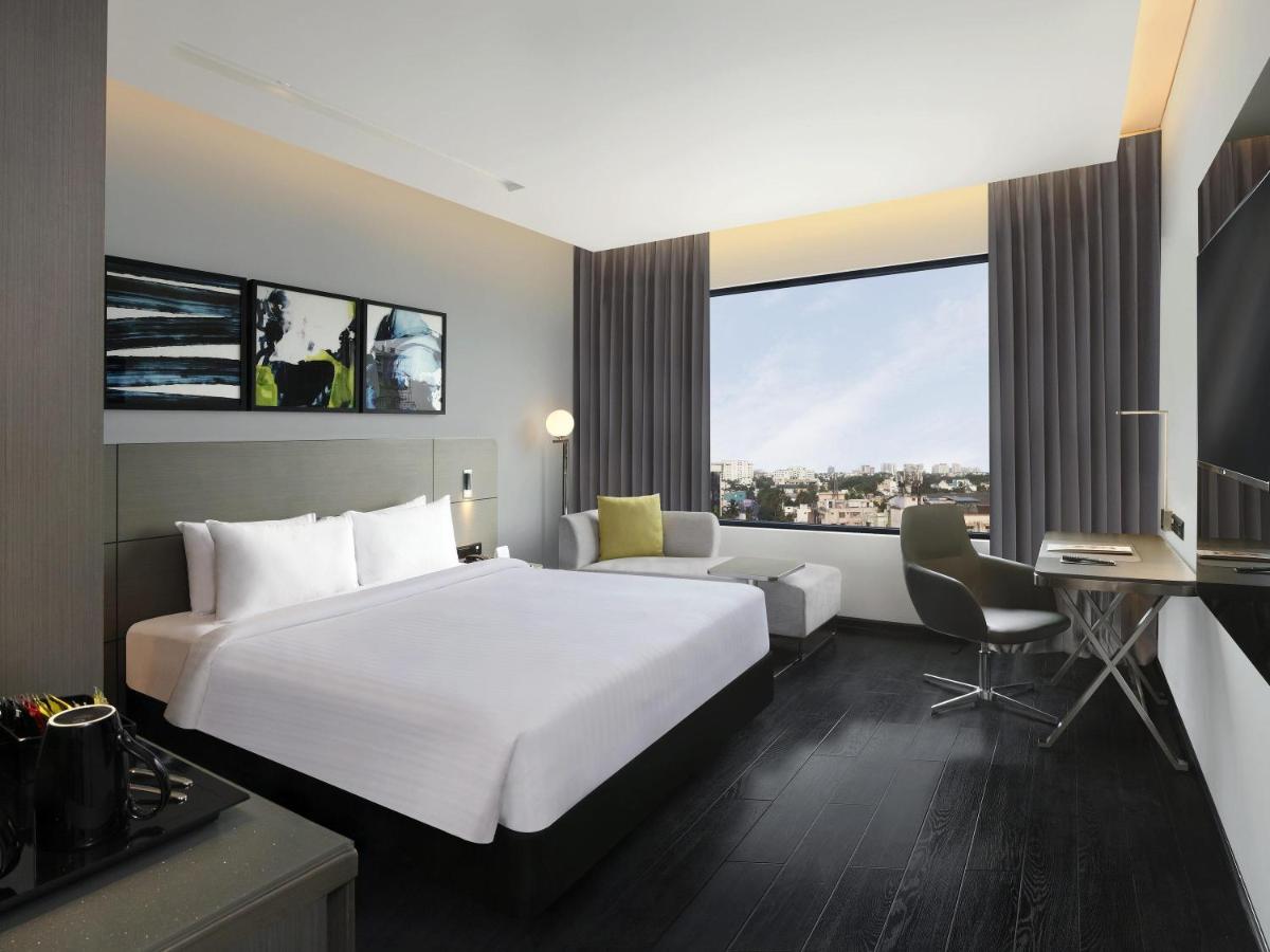 a hotel room with a large white bed and a desk at Novotel Chennai Chamiers Road in Chennai