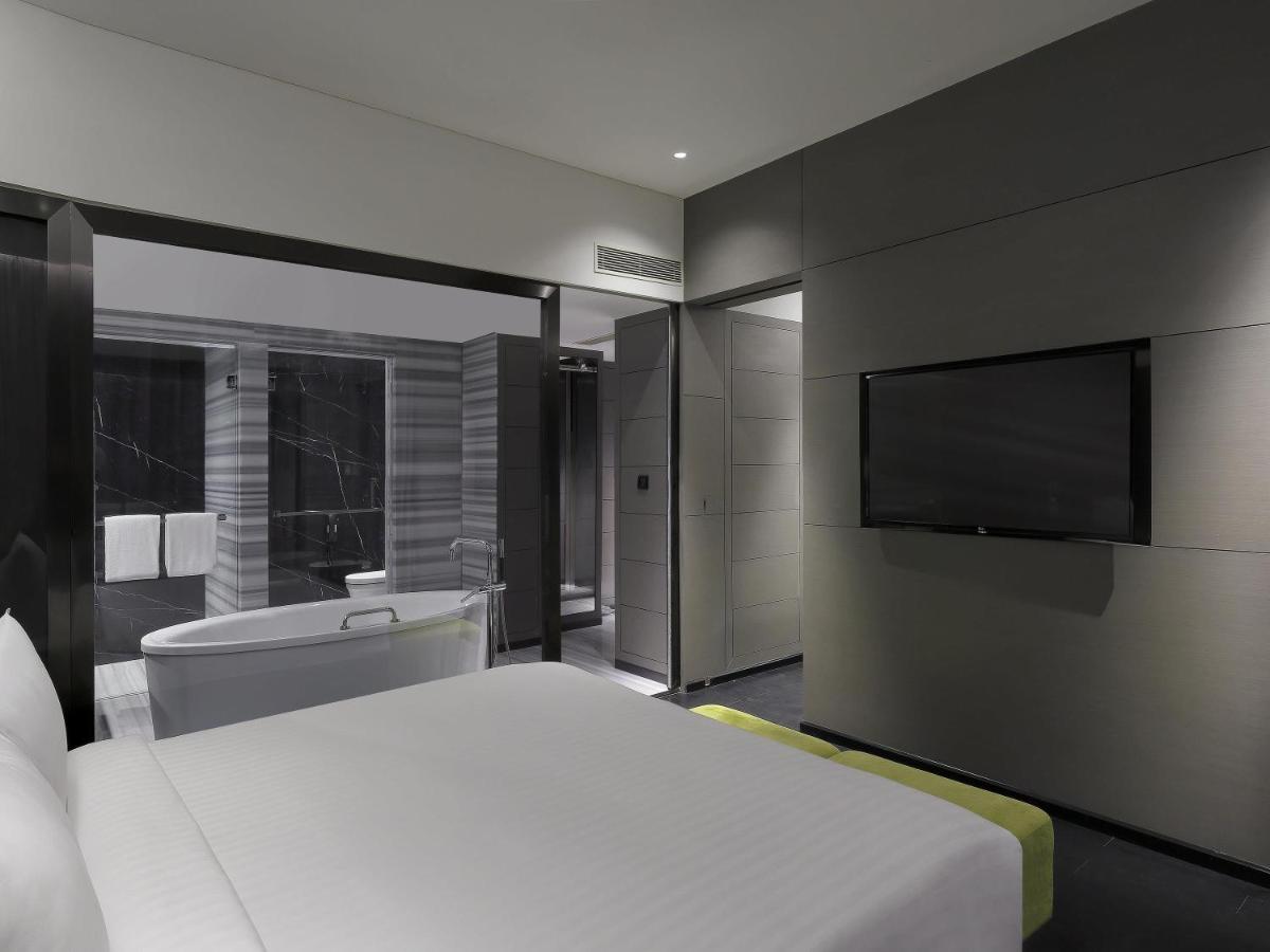 a bedroom with a bed and a tv and a tub at Novotel Chennai Chamiers Road in Chennai