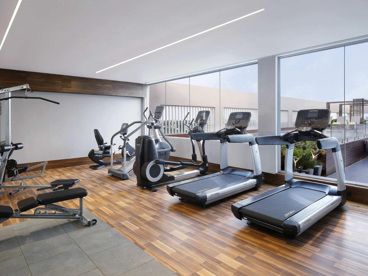 a gym with several treadmills and elliptical machines at Novotel Chennai Chamiers Road in Chennai
