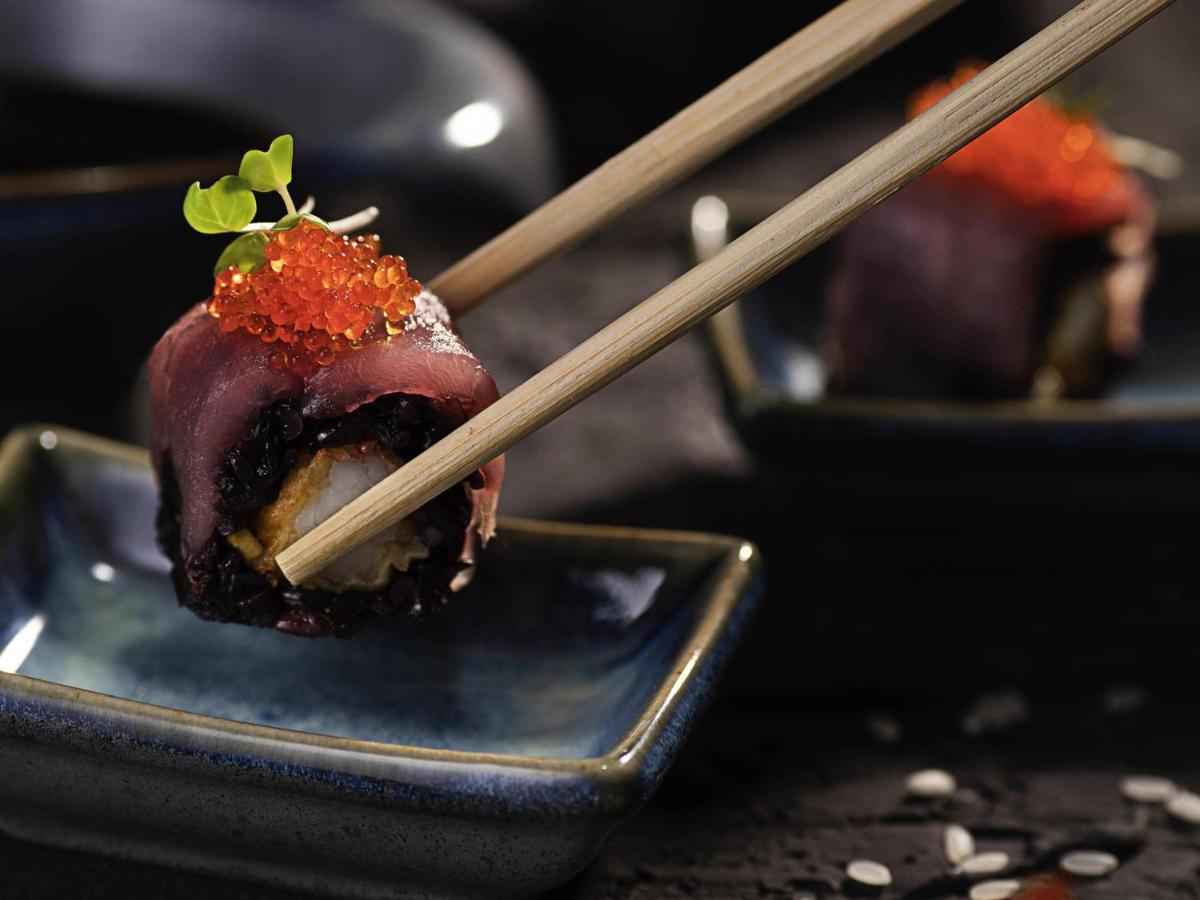 a piece of sushi on a blue plate with chopsticks at Novotel Chennai Chamiers Road in Chennai