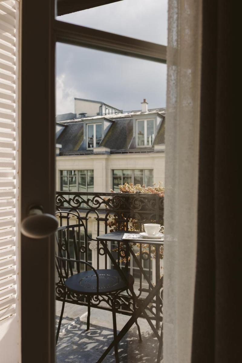 une table et des chaises sur un balcon avec vue sur un immeuble dans l'établissement Hotel Bachaumont, à Paris