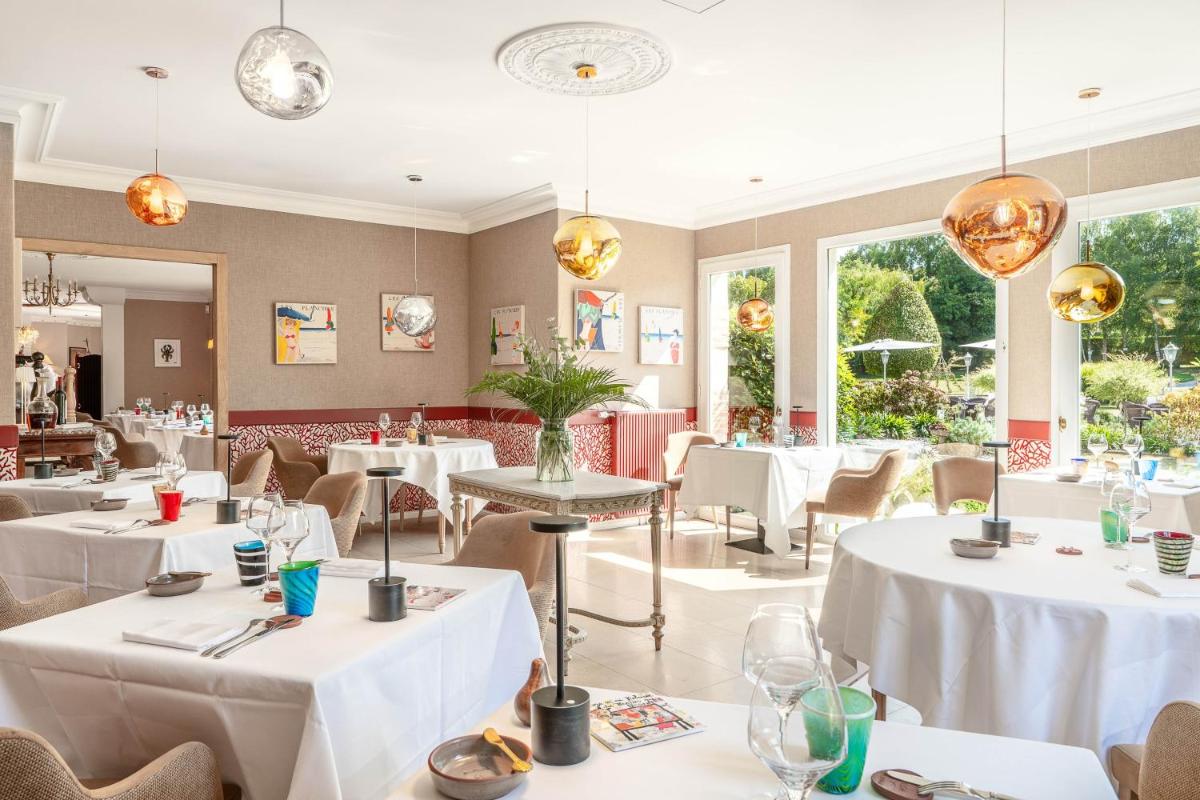 un restaurant avec des tables et des chaises blanches et des fenêtres dans l'établissement Le Manoir De La Poterie & Spa, à Cricquebœuf