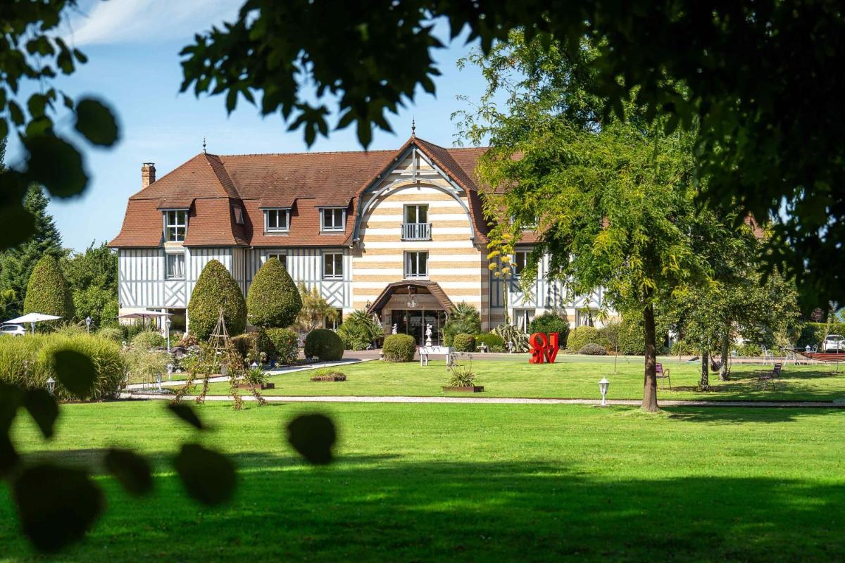 une grande maison avec un jardin recouvert de gazon vert dans l'établissement Le Manoir De La Poterie & Spa, à Cricquebœuf