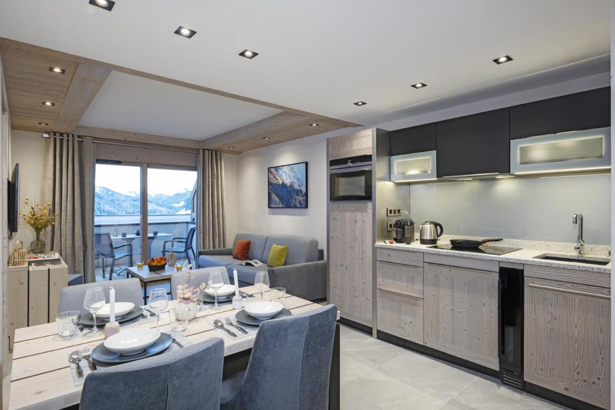 une cuisine et un salon avec une table et des chaises dans l'établissement MGM Hôtels & Résidences - Résidence Chalets de Joy, au Grand-Bornand