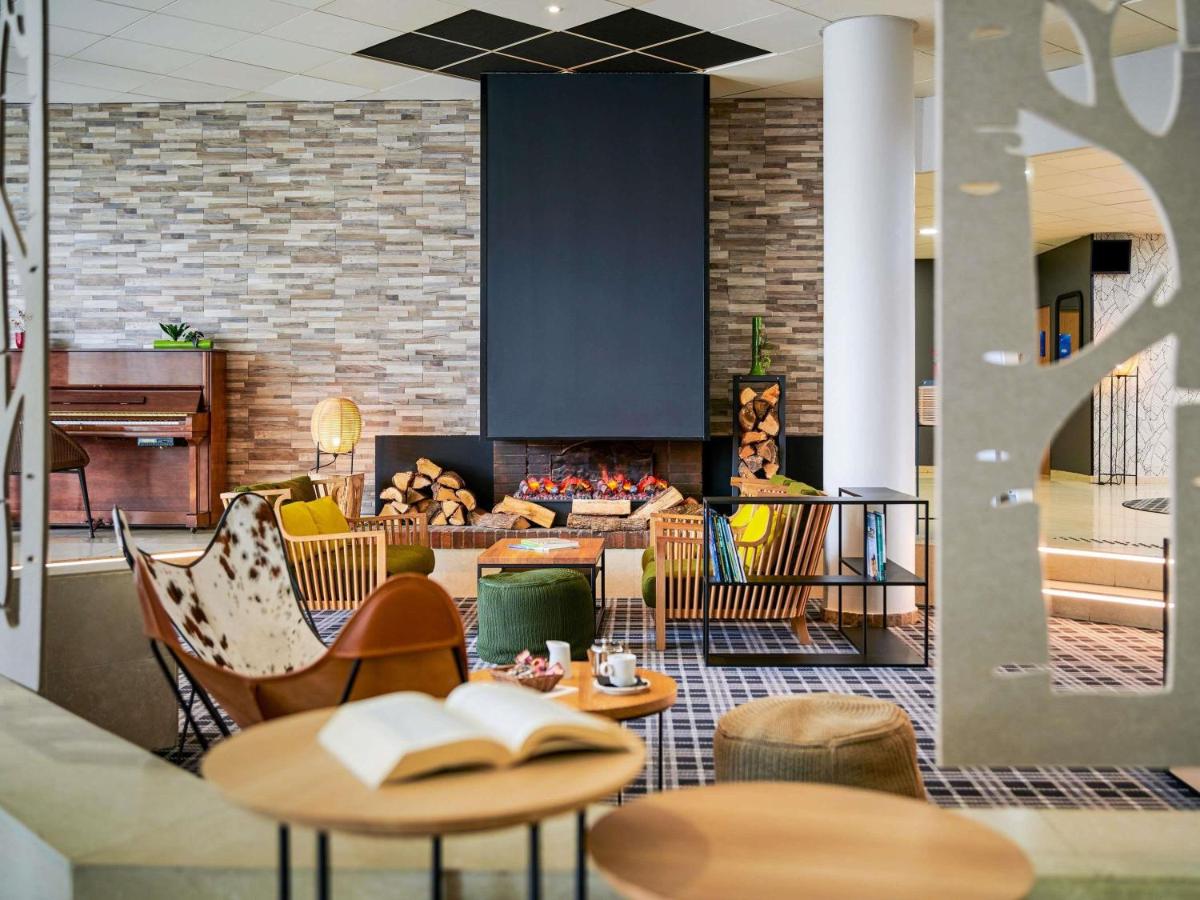un hall d'entrée avec des tables et des chaises et une cheminée dans l'établissement Novotel Senart Golf De Greenparc, à Saint-Pierre-du-Perray