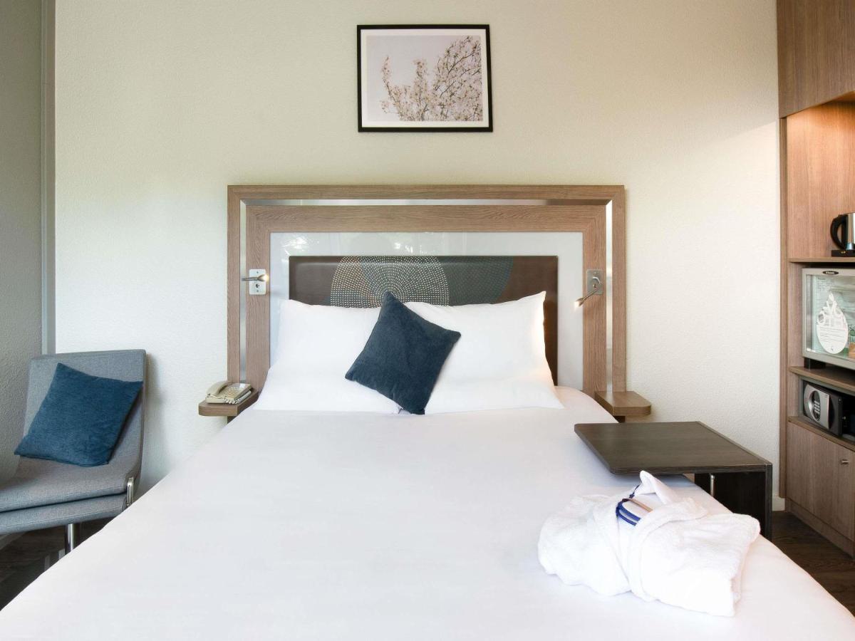 une chambre avec un grand lit blanc et des oreillers bleus dans l'établissement Novotel Senart Golf De Greenparc, à Saint-Pierre-du-Perray