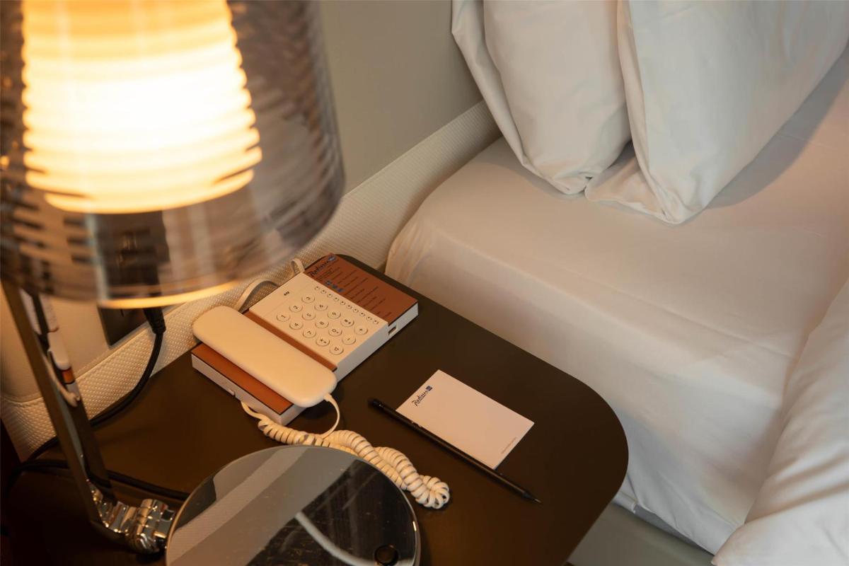 un lit avec une table avec un téléphone et un livre dans l'établissement Radisson Blu Hotel Bordeaux, à Bordeaux