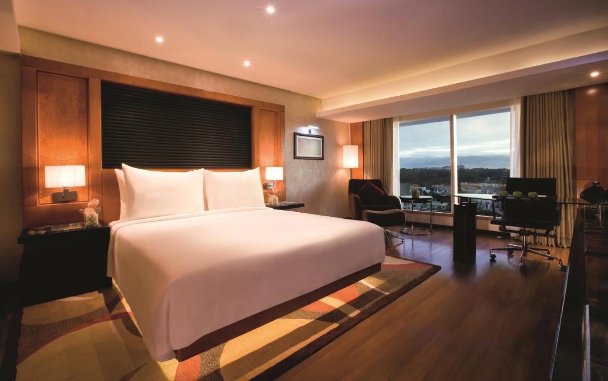 a bedroom with a large bed and a desk and a room with a desk at Gokulam Grand Hotel & Spa Bangalore in Bengaluru a bedroom with a large bed and a desk and a room with a desk at Gokulam Grand Hotel & Spa Bangalore in Bengaluru