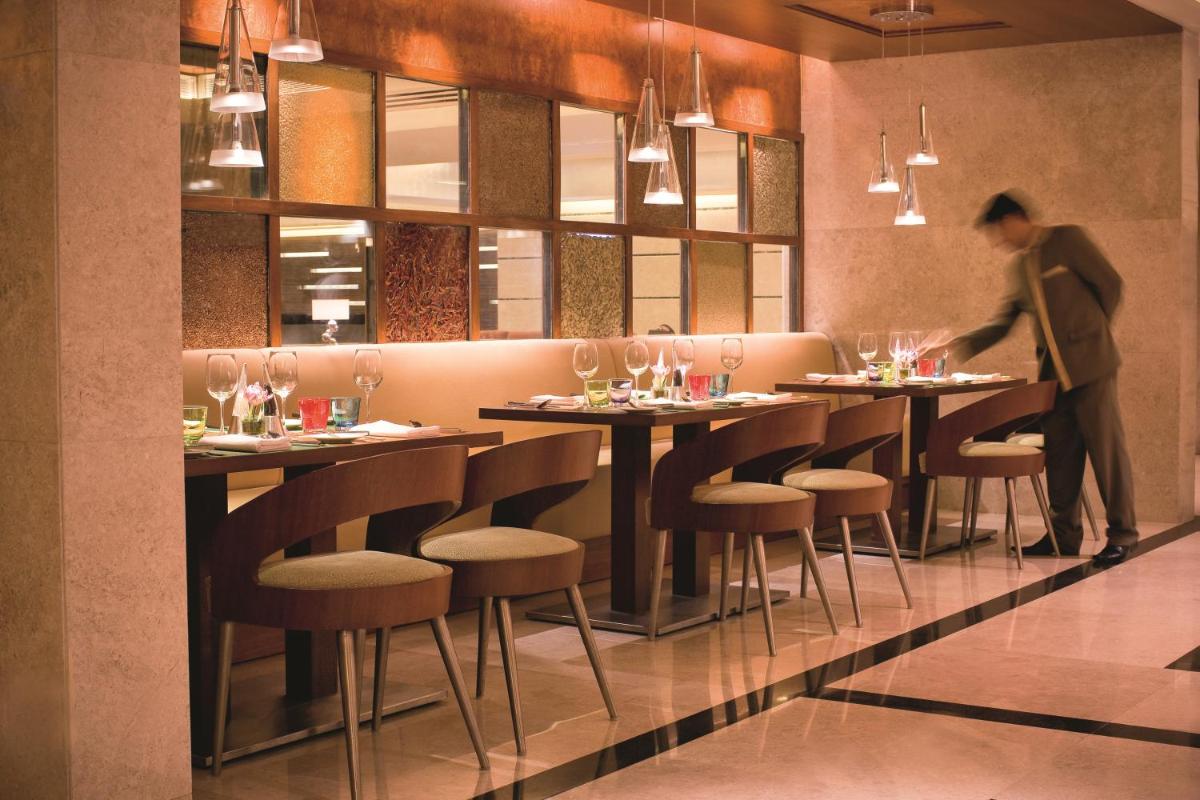 a man standing in a restaurant with tables and chairs at Gokulam Grand Hotel & Spa Bangalore in Bengaluru a man standing in a restaurant with tables and chairs at Gokulam Grand Hotel & Spa Bangalore in Bengaluru
