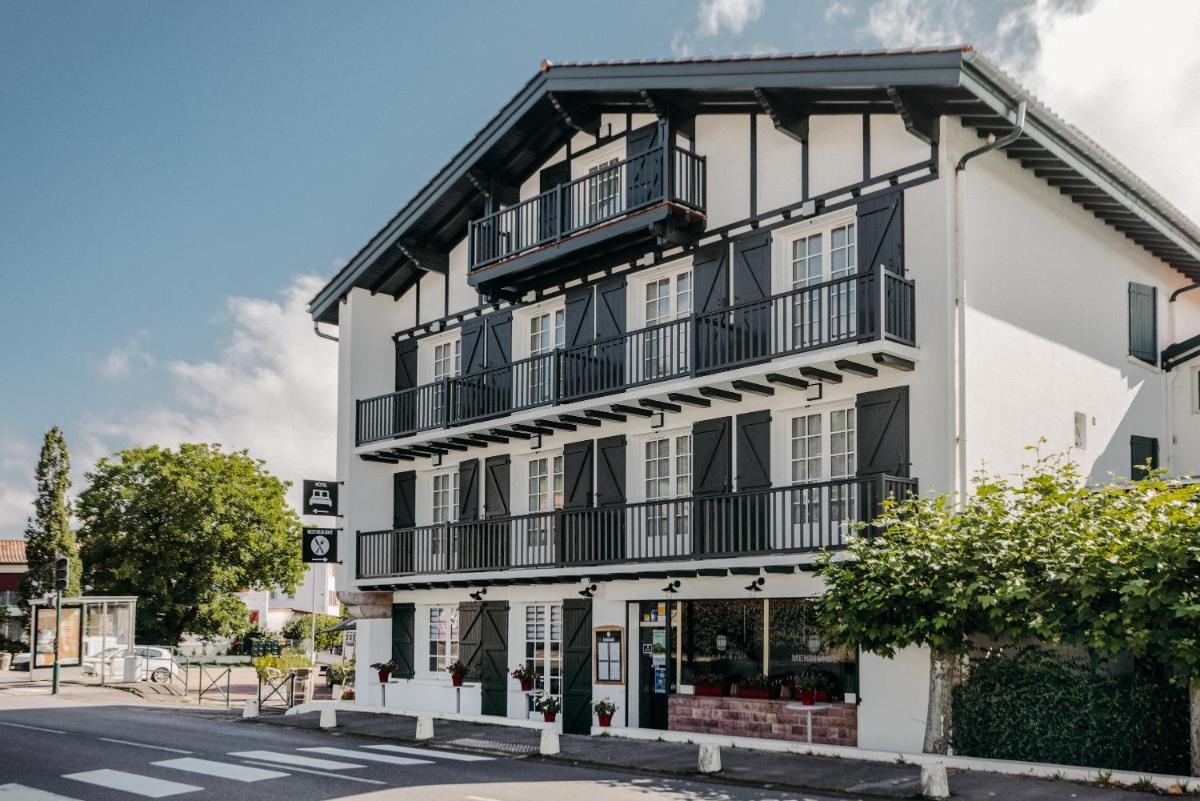 un bâtiment blanc avec des balcons noirs et une rue dans l'établissement Hotel Trinquet, à Saint-Pée-sur-Nivelle