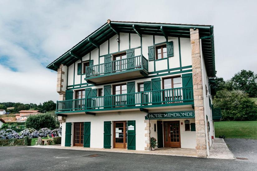 un immeuble blanc et vert avec un balcon dans l'établissement Hotel Mendionde, à Saint-Pée-sur-Nivelle