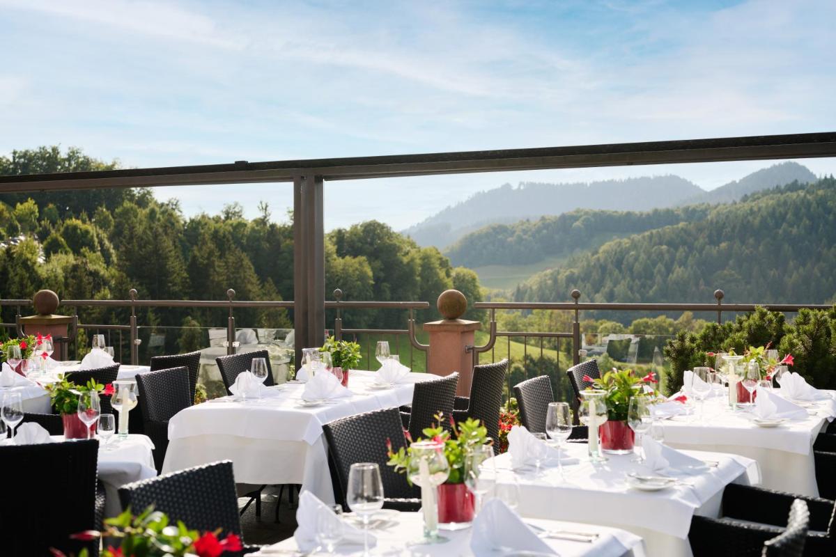 ein Restaurant mit weißen Tischen und Stühlen mit Bergen im Hintergrund in der Unterkunft Hotel Dollenberg in Bad Peterstal-Griesbach + 60 Fotos
