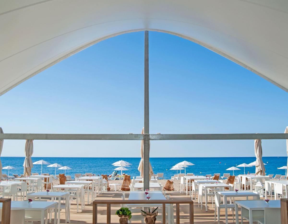 Una playa con mesas y sillas y el océano. en KAKTUS Hotel Kaktus Playa - Adults Recommended, en Calella