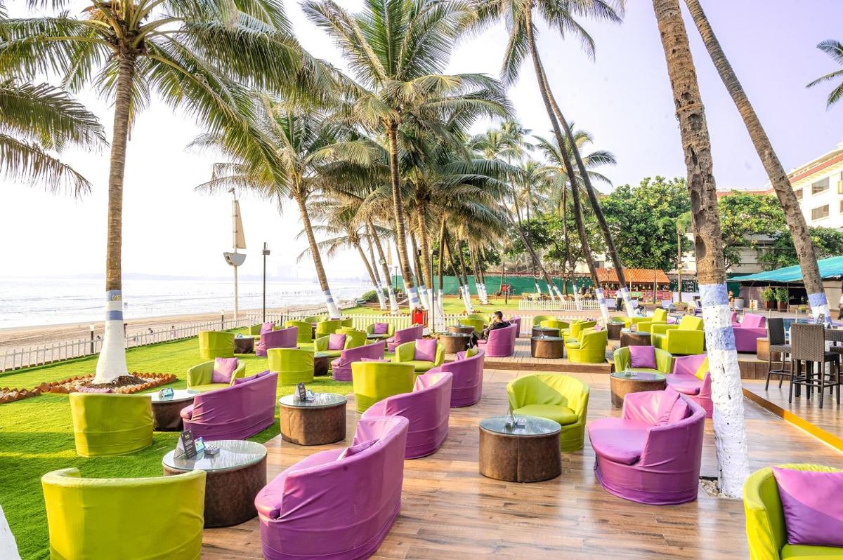 a restaurant with colorful chairs and palm trees on the beach at Novotel Mumbai Juhu Beach in Mumbai