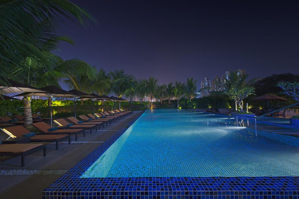 a swimming pool with lounge chairs and palm trees at night at The Westin Mumbai Garden City in Mumbai a swimming pool with lounge chairs and palm trees at night at The Westin Mumbai Garden City in Mumbai