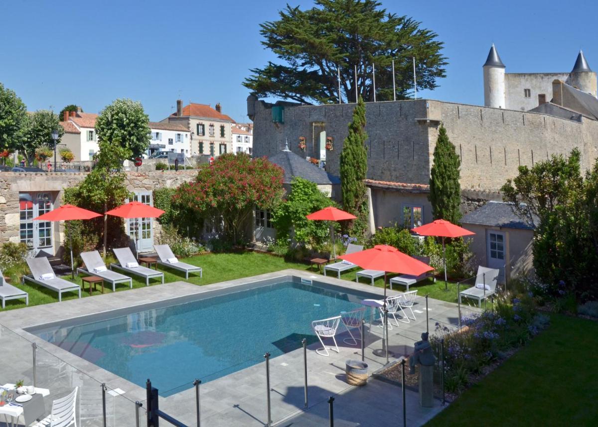 - une piscine avec des parasols et des chaises rouges dans l'établissement Le Général d'Elbée Hotel & Spa - Teritoria, à Noirmoutier-en-l'lle