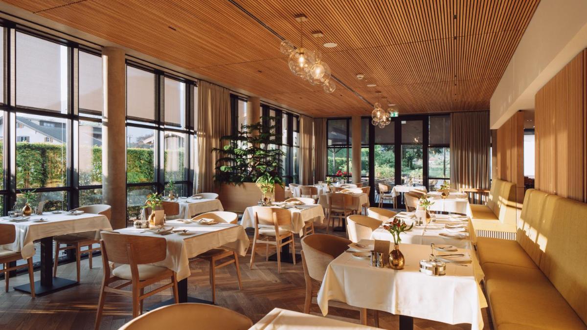 ein Restaurant mit weißen Tischen und Stühlen und Fenstern in der Unterkunft Parkhotel Egerner Höfe in Rottach-Egern