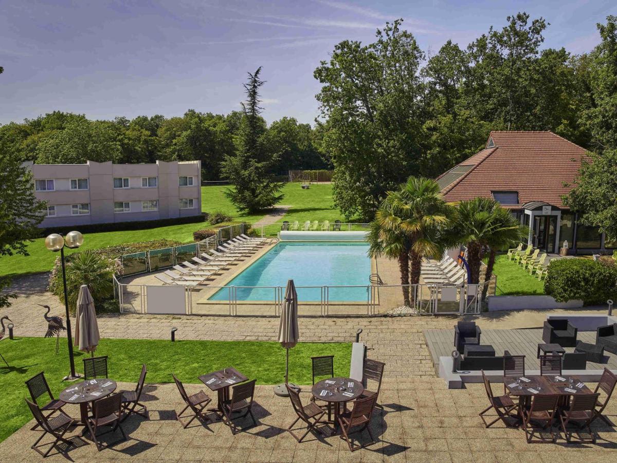 une piscine avec tables et chaises à côté d'un bâtiment dans l'établissement Novotel Fontainebleau Ury, à Ury