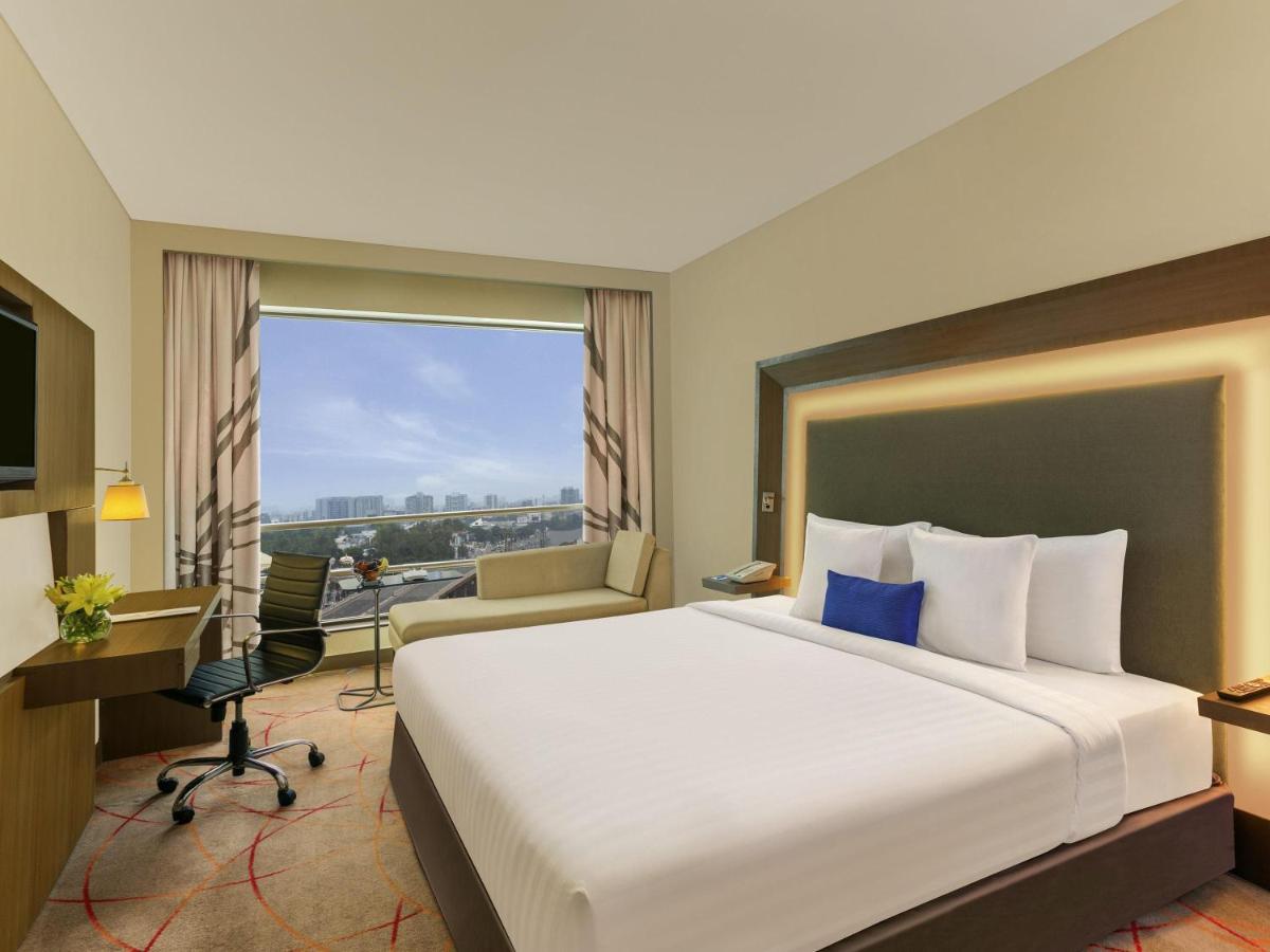 a hotel room with a bed and a desk and a window at Novotel Ahmedabad in Ahmedabad