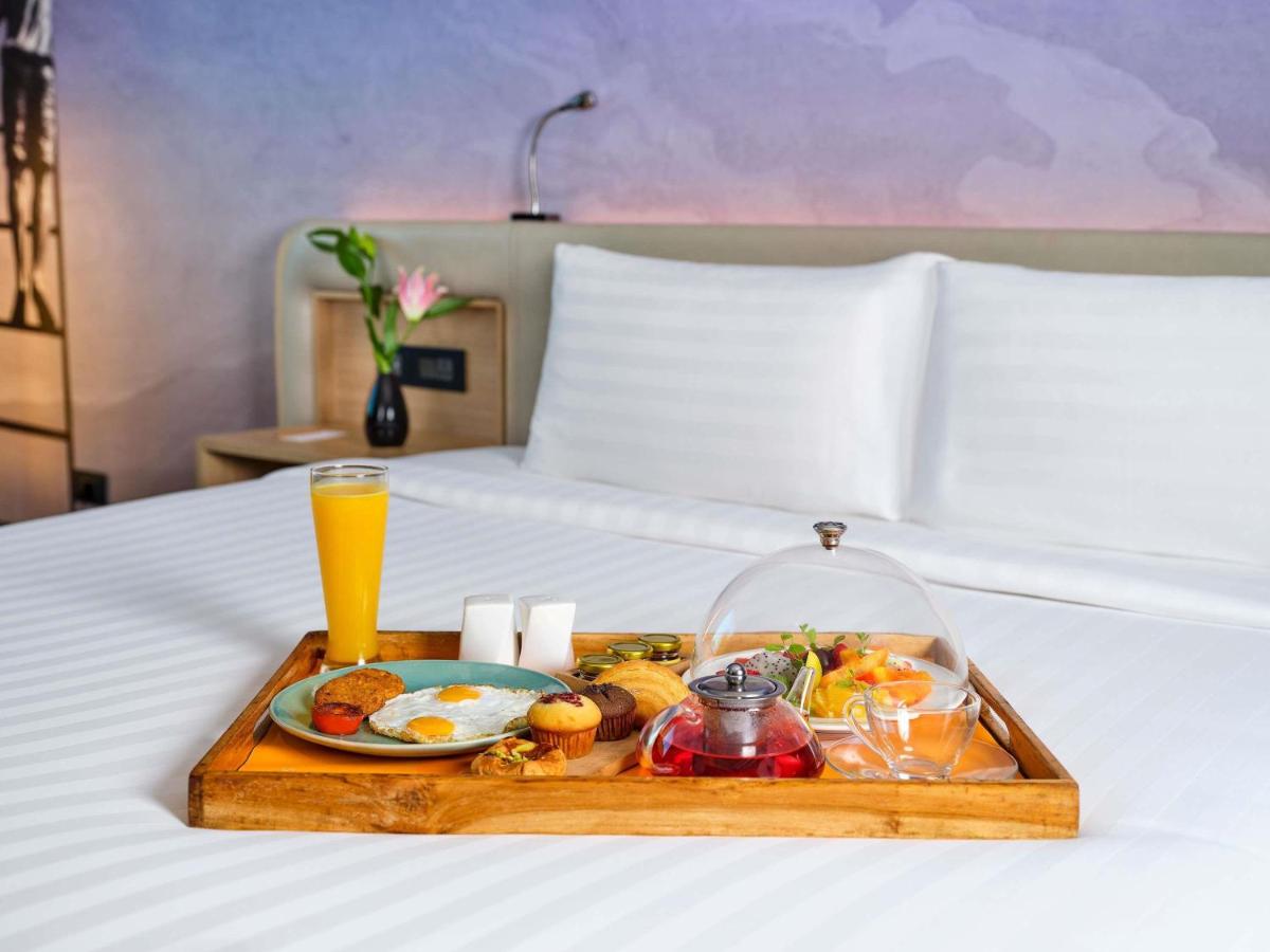 a tray of food on a bed with a drink at Novotel Ahmedabad in Ahmedabad