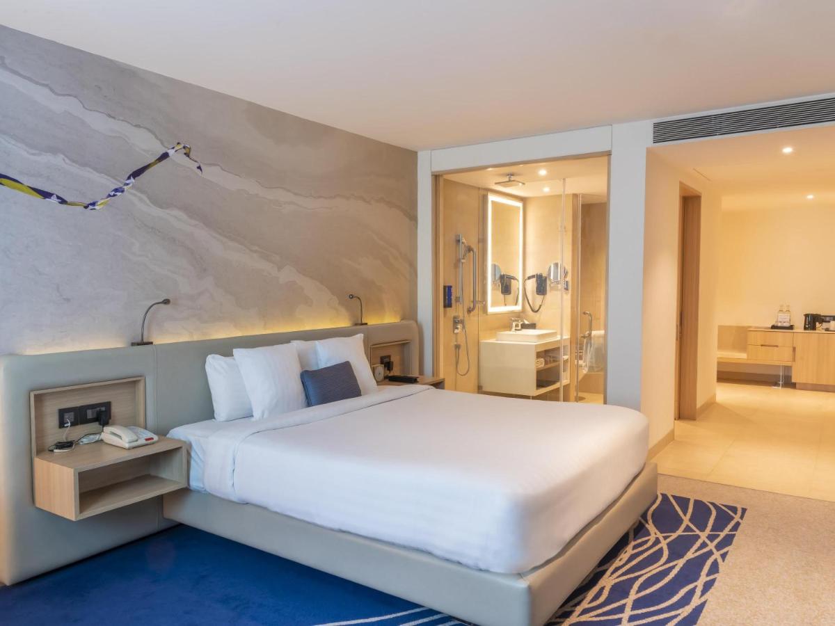 a bedroom with a large white bed and a bathroom at Novotel Ahmedabad in Ahmedabad