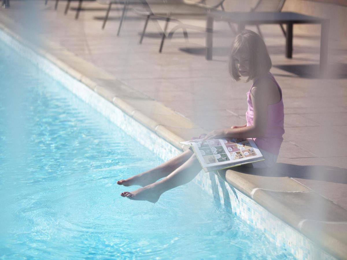 a young girl sitting next to a swimming pool at Novotel Ahmedabad in Ahmedabad