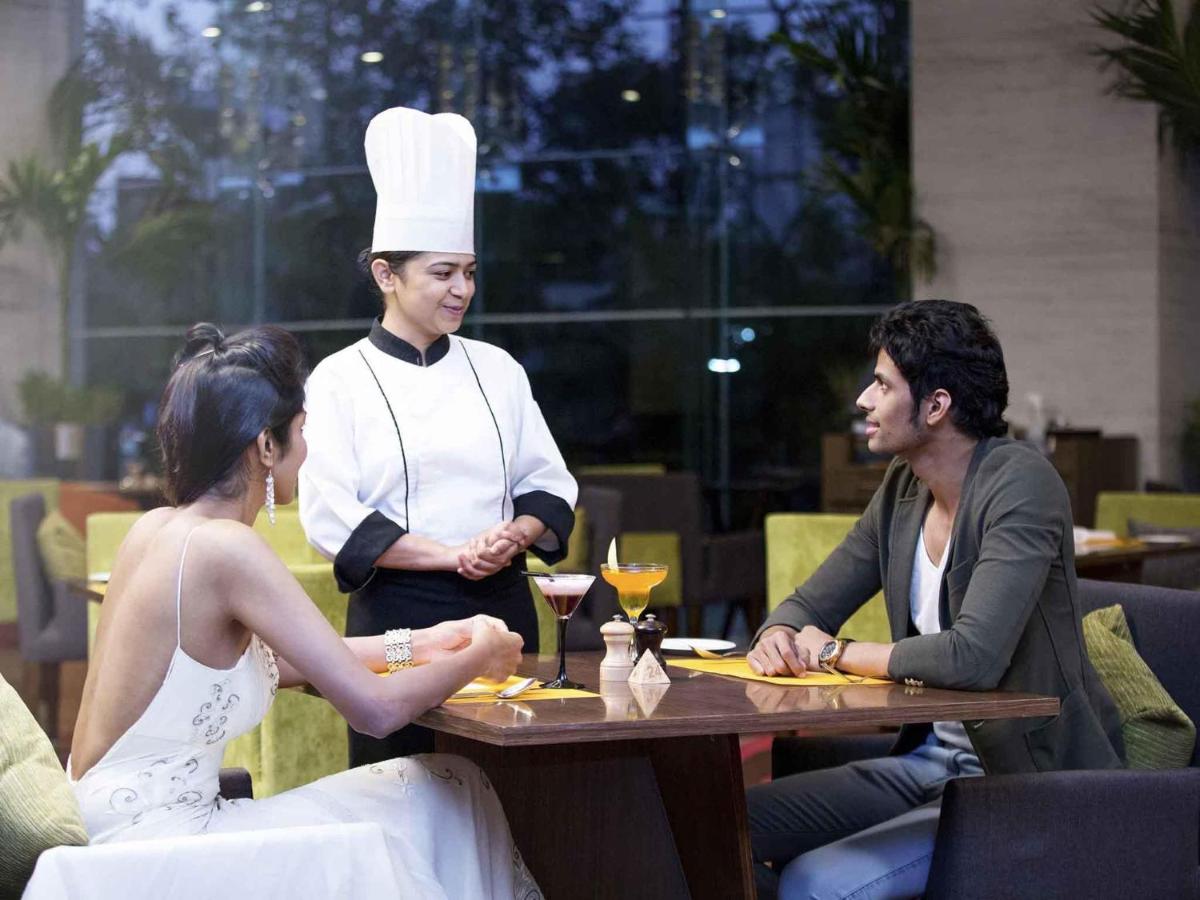a woman sitting at a table in a restaurant with a chef at Novotel Ahmedabad in Ahmedabad