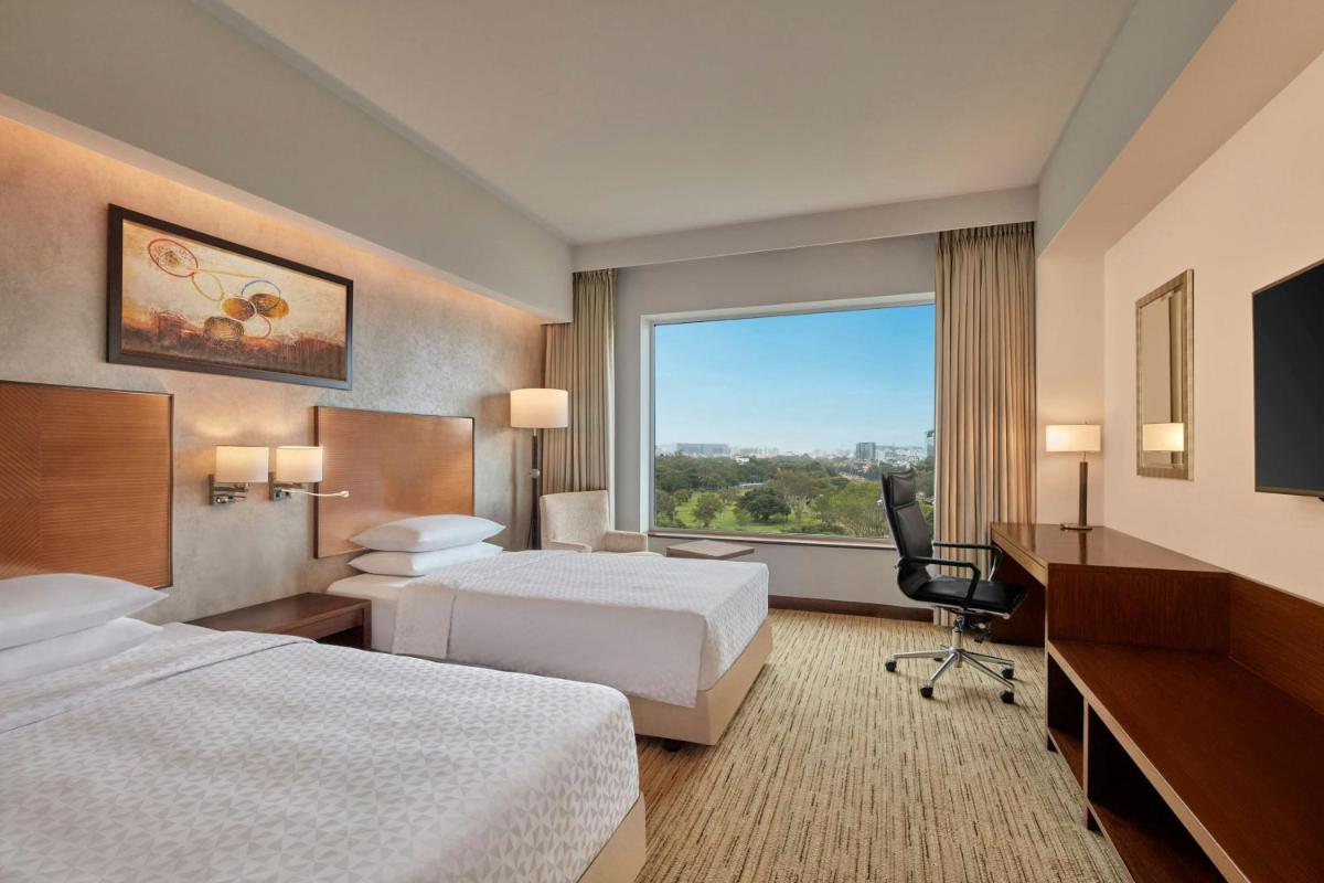 a hotel room with two beds and a desk and a window at Four Points by Sheraton Hotel and Serviced Apartments Pune in Pune