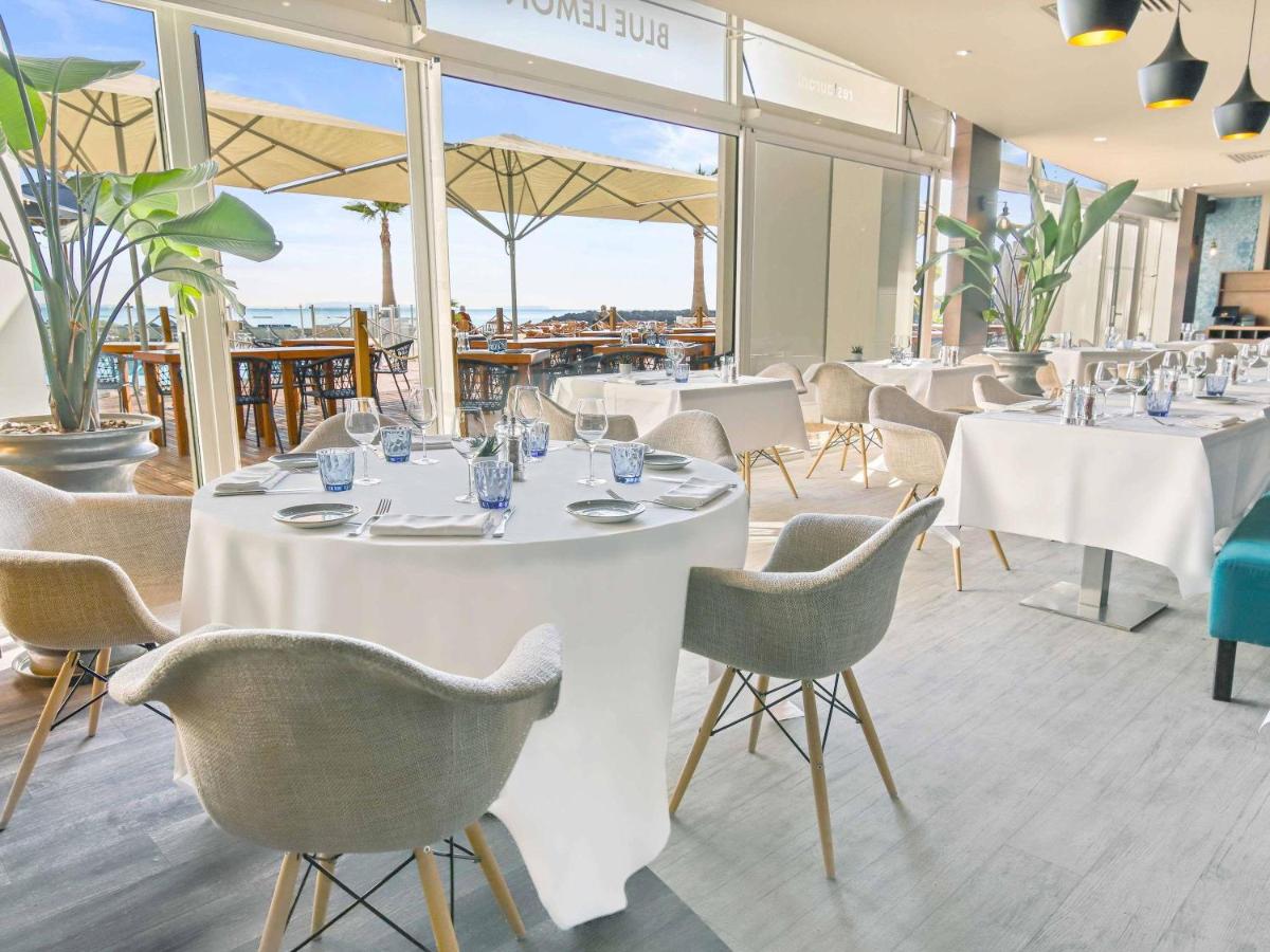 un restaurant avec des tables et des chaises blanches et des fenêtres dans l'établissement Pullman Cannes Mandelieu, à Mandelieu-la-Napoule
