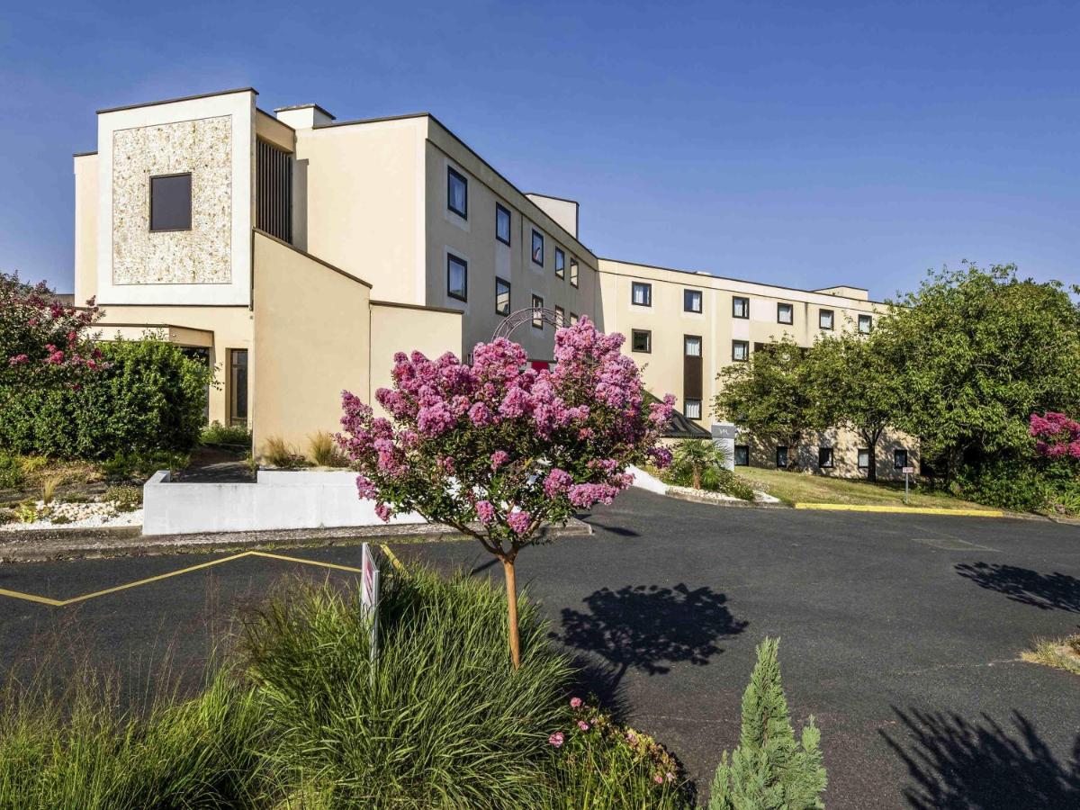 un bâtiment avec des fleurs violettes dans un parking dans l'établissement Mercure Tours Sud, à Joué-lès-Tours