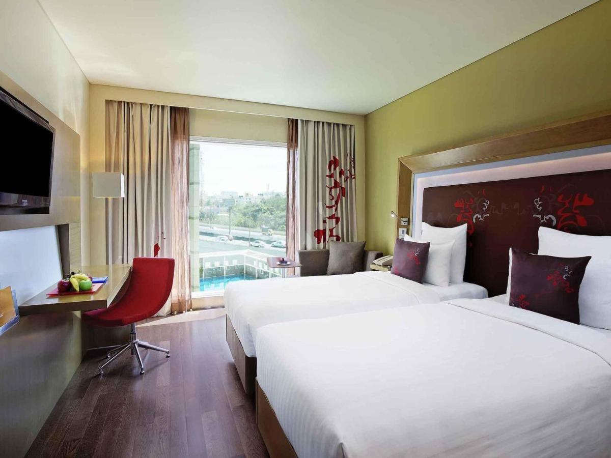 a hotel room with two beds and a window at Novotel Bengaluru Outer Ring Road in Bengaluru