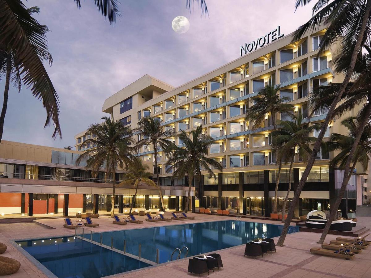 a hotel with a swimming pool and palm trees at Novotel Mumbai Juhu Beach in Mumbai