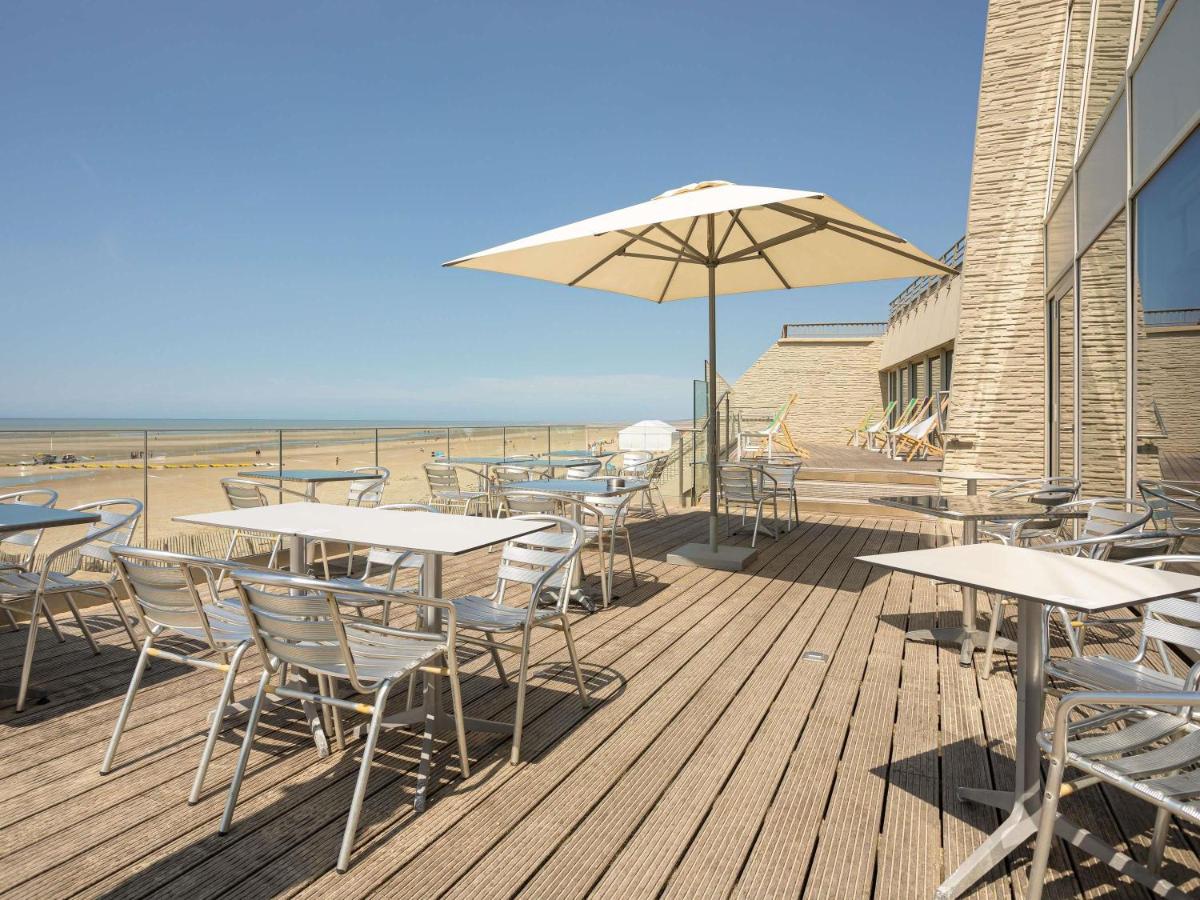 une terrasse avec tables, chaises et parasol sur la plage dans l'établissement ibis Thalassa Le Touquet, à Le Touquet-Paris-Plage