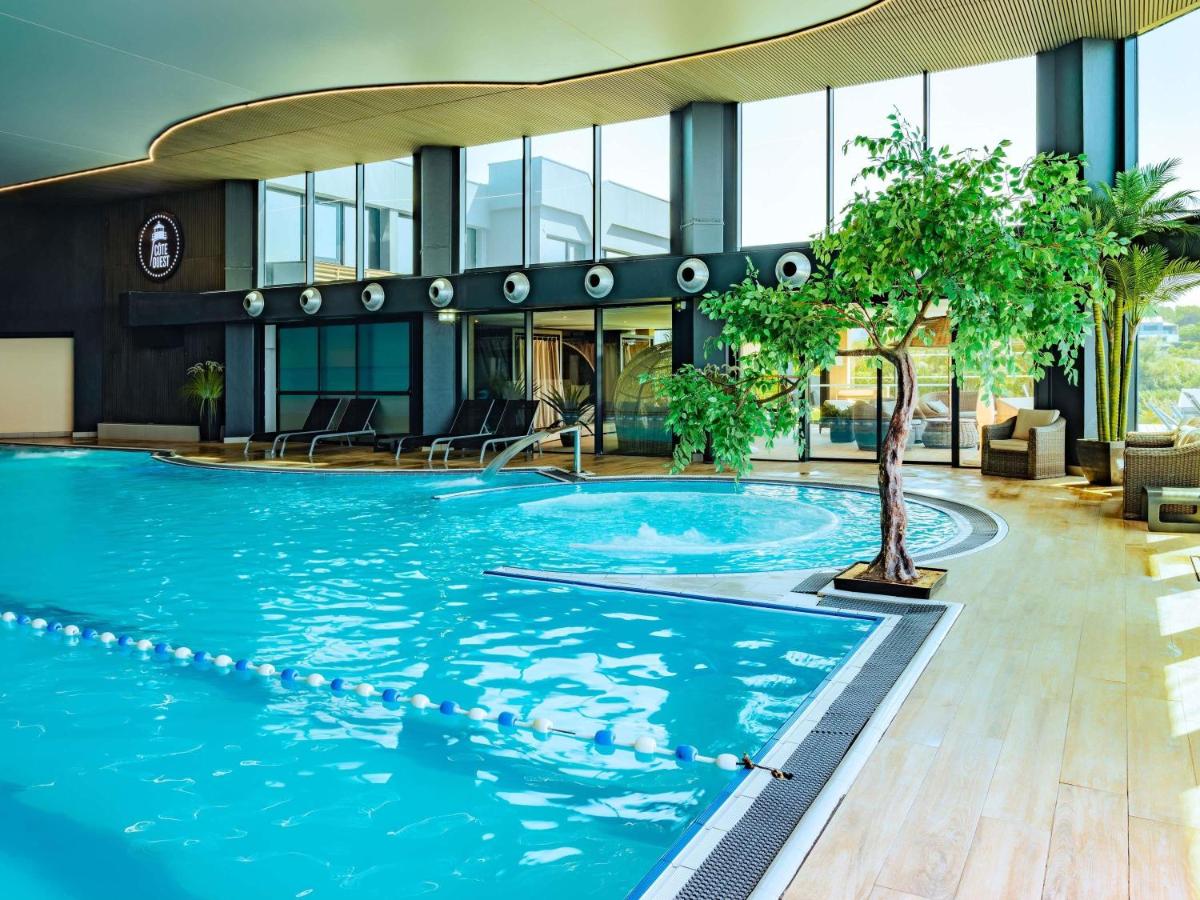 une piscine dans un bâtiment avec un arbre au milieu dans l'établissement Côte Ouest Thalasso & Spa Les Sables d'Olonne - MGallery Collection, à Les Sables-dʼOlonne