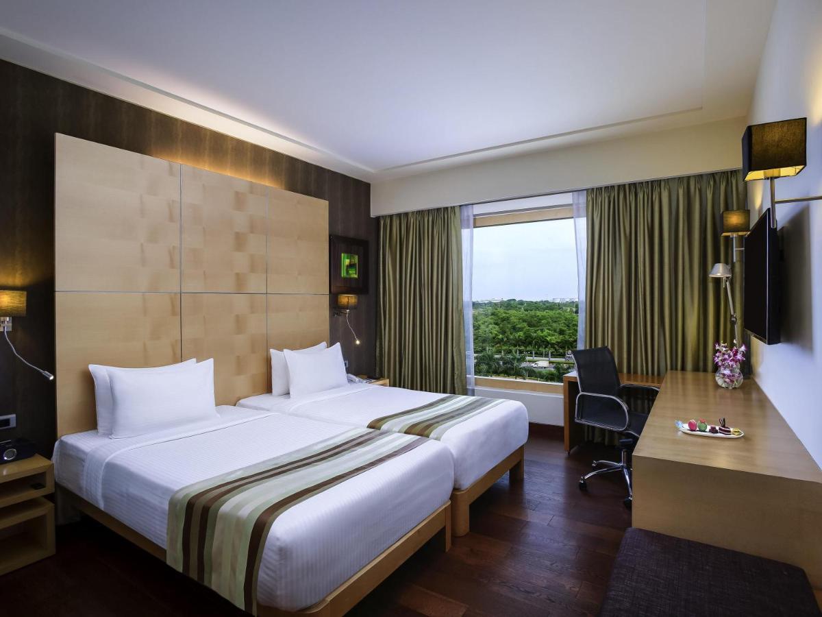 a hotel room with a bed and a desk and a window at Novotel Hyderabad Airport in Hyderabad a hotel room with a bed and a desk and a window at Novotel Hyderabad Airport in Hyderabad