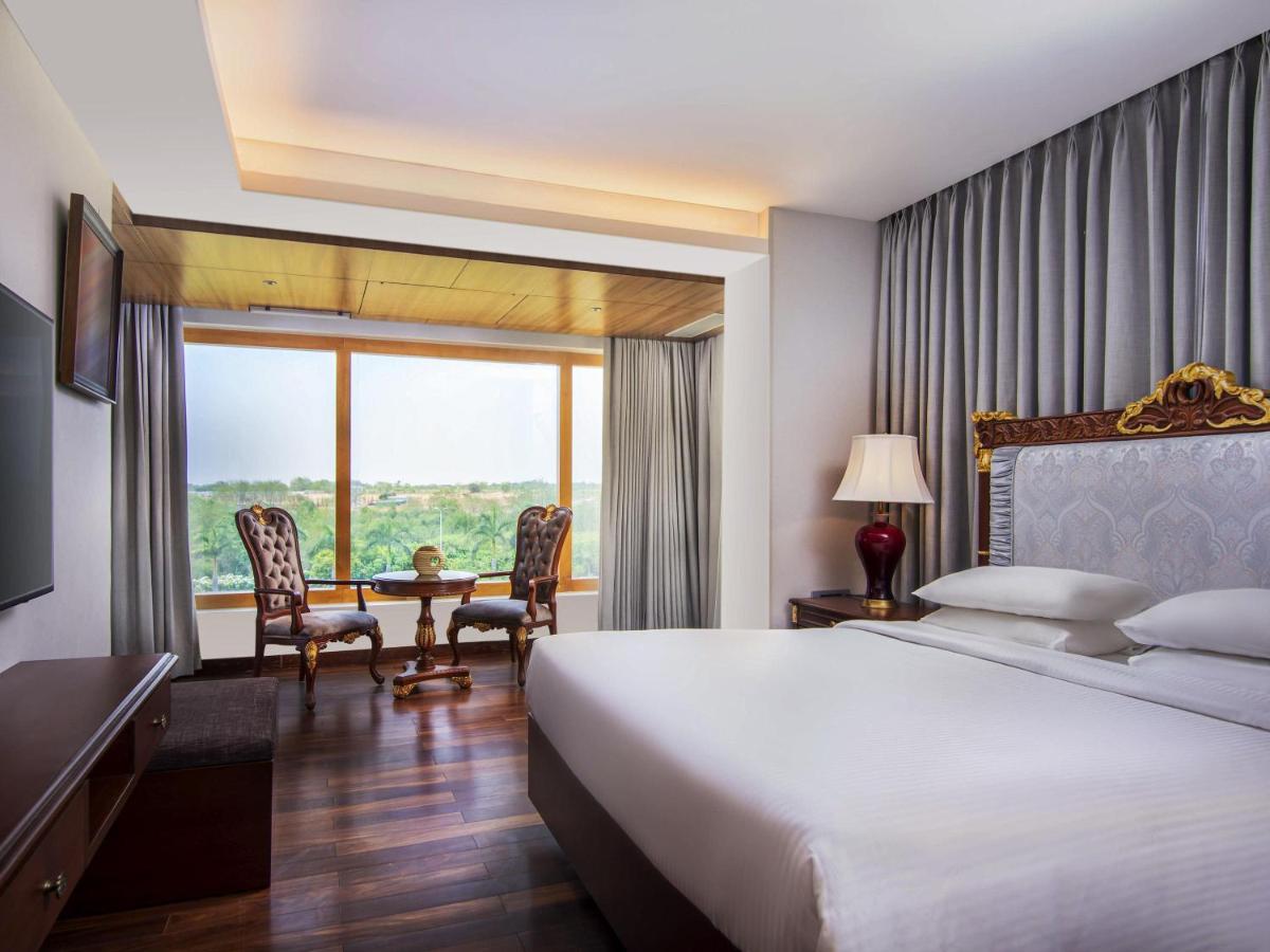 a hotel room with a bed and a table with chairs at Novotel Hyderabad Airport in Hyderabad