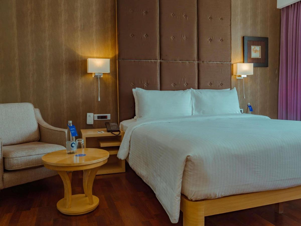 a bedroom with a large bed and a chair at Novotel Hyderabad Airport in Hyderabad
